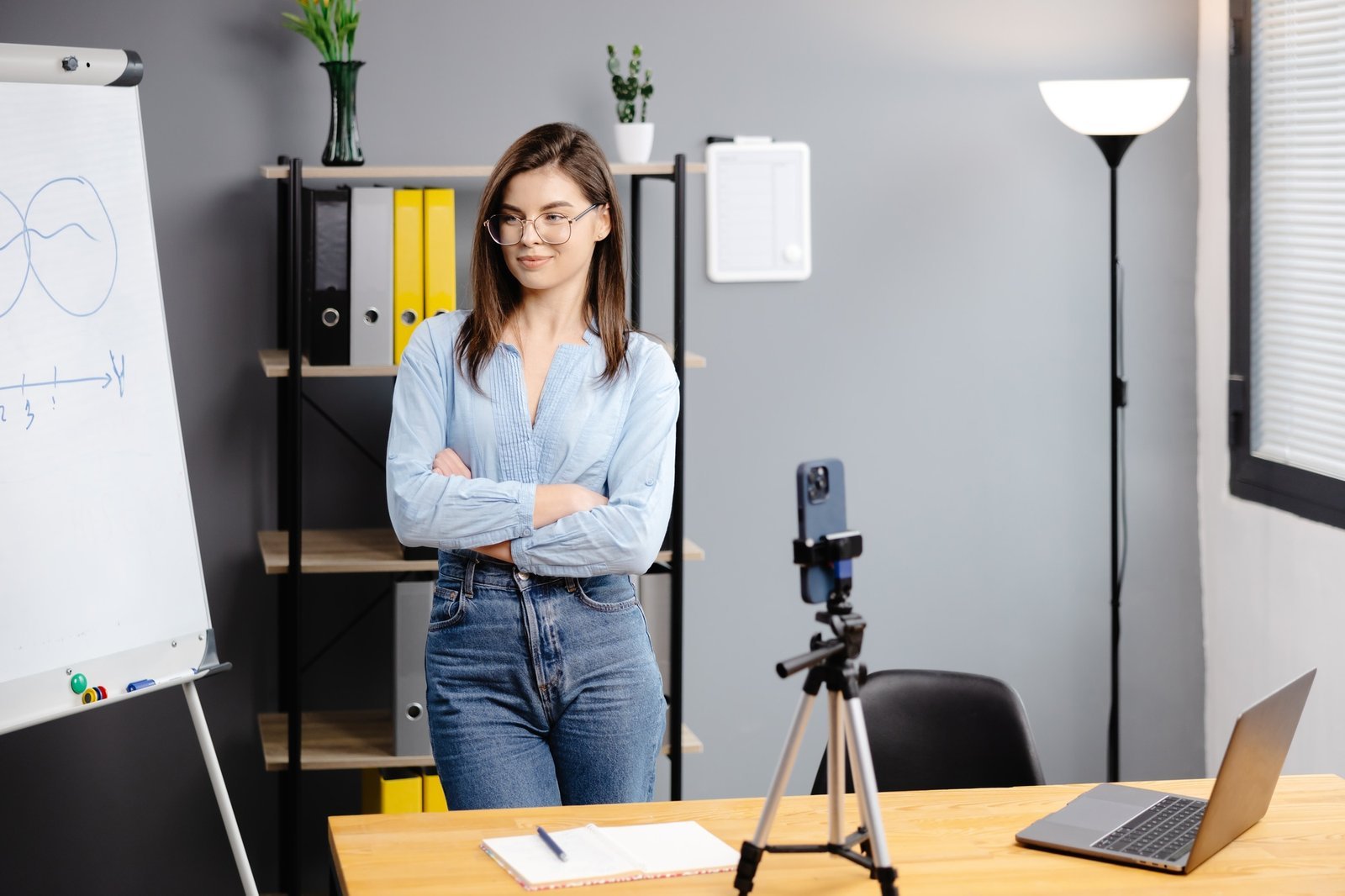 Young woman mentor recording presentation, webinar on smartphone standing on tripod